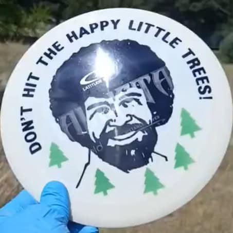 024001.07 Gold Line Ballista Bob Ross Don't Hit The Happy Little Trees ghost stamp disc golf distance driver from Latitude 64 front view sunlight